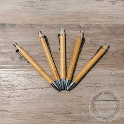 Set of wooden pens on a wooden surface with a brand logo in the corner.