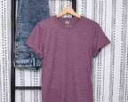 Purple t-shirt on a hanger with blue jeans stacked behind against a patterned wall.