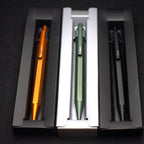 Three pens in a holder with orange, green, and black colors on a dark background.