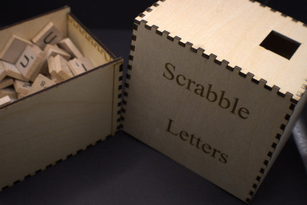 Wooden box labeled 'Scrabble Letters' with letter tiles inside on a dark surface